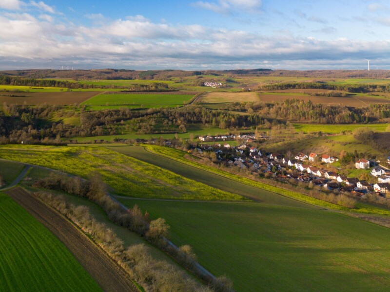 Eine lebendige Luftaufnahme der Landschaft in der Nähe von Bad Mergentheim mit üppigen grünen Feldern und einem klaren blauen Himmel
